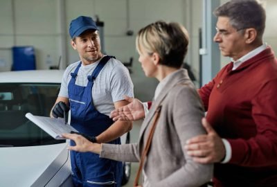 Happy auto repairman and couple analyzing data while communicating in a workshop.